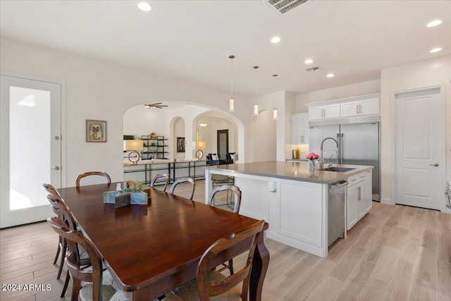 kitchen featuring a center island with sink, white cabinets, hanging light fixtures, light wood-type flooring, and appliances with stainless steel finishes