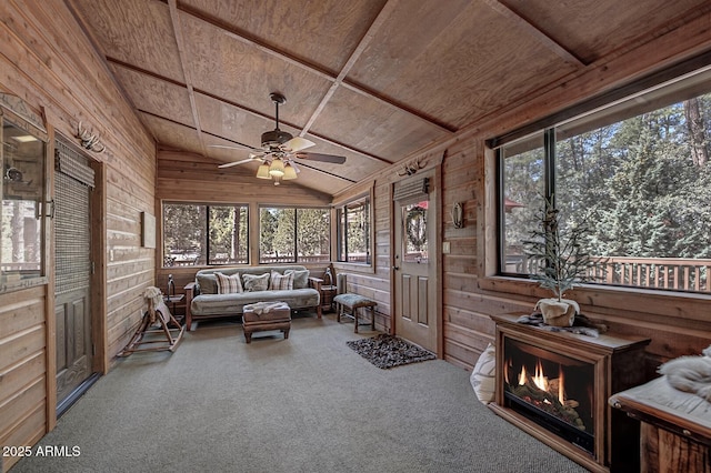 carpeted living room with lofted ceiling, wooden ceiling, wood walls, and ceiling fan