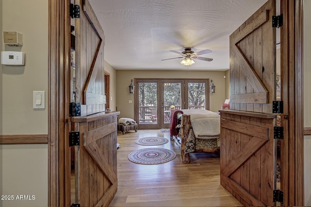 entrance foyer with a textured ceiling, french doors, a barn door, light wood finished floors, and ceiling fan