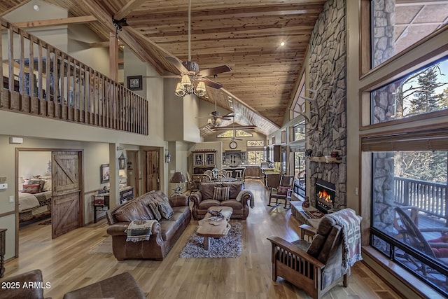 living area featuring high vaulted ceiling, a ceiling fan, wood finished floors, a stone fireplace, and wood ceiling