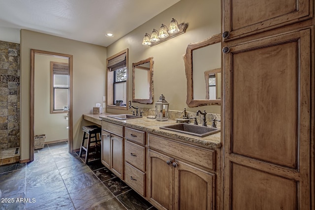 bathroom with double vanity, tiled shower, baseboards, and a sink