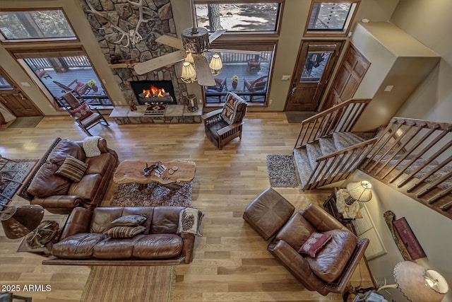 living area featuring a stone fireplace, stairway, a high ceiling, and wood finished floors