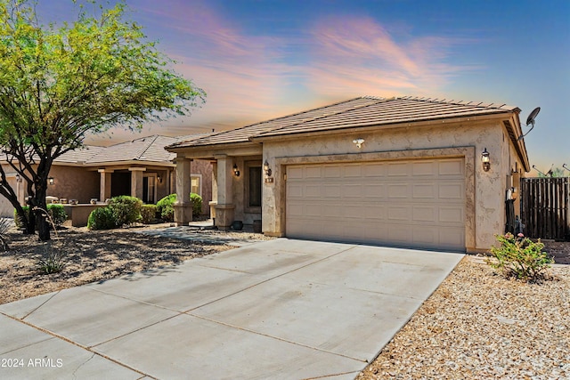 ranch-style home featuring a garage, concrete driveway, a tile roof, fence, and stucco siding