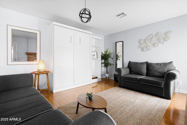 living room with built in shelves, a notable chandelier, and light hardwood / wood-style flooring