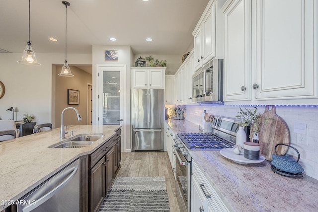 kitchen with light stone counters, stainless steel appliances, a sink, white cabinets, and light wood finished floors