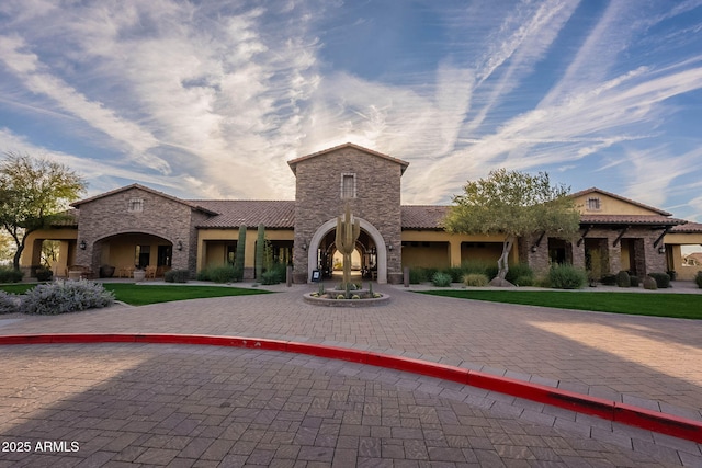 mediterranean / spanish house with stone siding, decorative driveway, a tile roof, and stucco siding