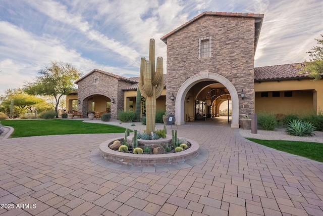 exterior space with a tile roof, curved driveway, stucco siding, stone siding, and a front lawn