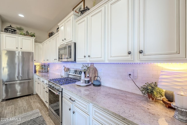 kitchen featuring light stone countertops, white cabinetry, stainless steel appliances, and decorative backsplash