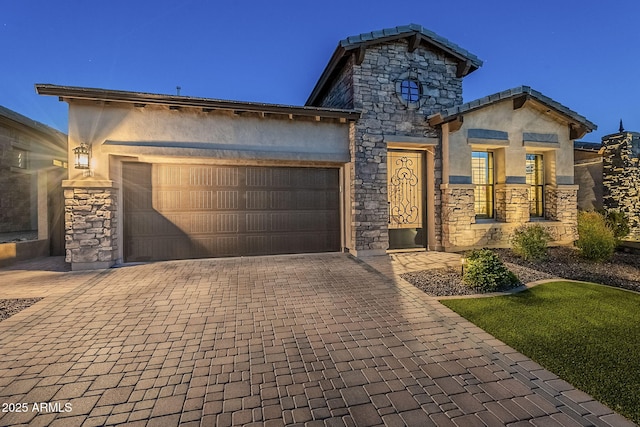 view of front of home featuring decorative driveway, stone siding, an attached garage, and stucco siding