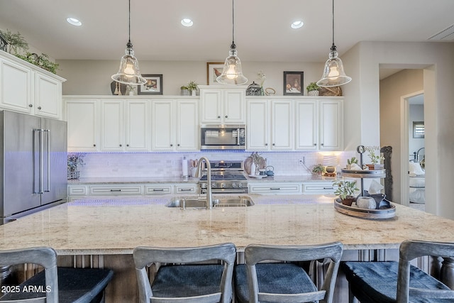 kitchen featuring a sink, white cabinets, hanging light fixtures, appliances with stainless steel finishes, and decorative backsplash