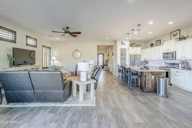 living room with light wood-style flooring, arched walkways, ceiling fan, and recessed lighting