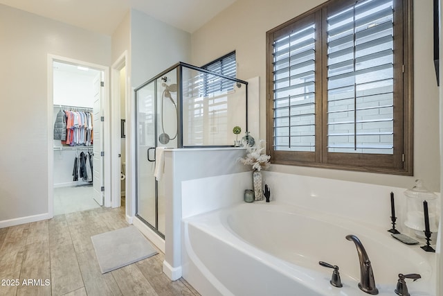 bathroom featuring a spacious closet, wood finished floors, a garden tub, and a shower stall