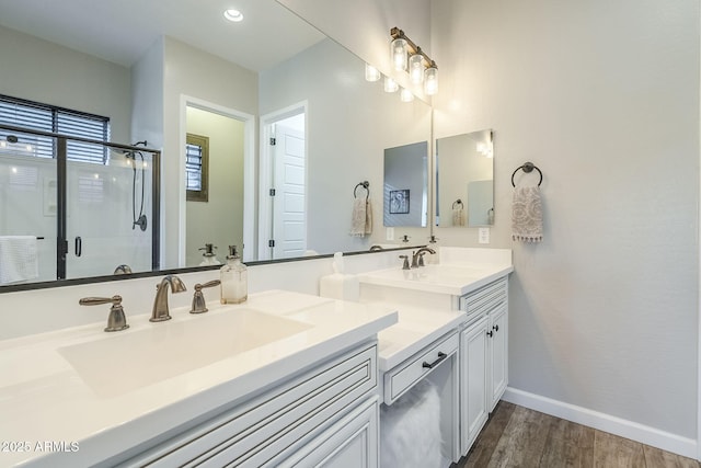 bathroom featuring double vanity, a stall shower, a sink, wood finished floors, and baseboards