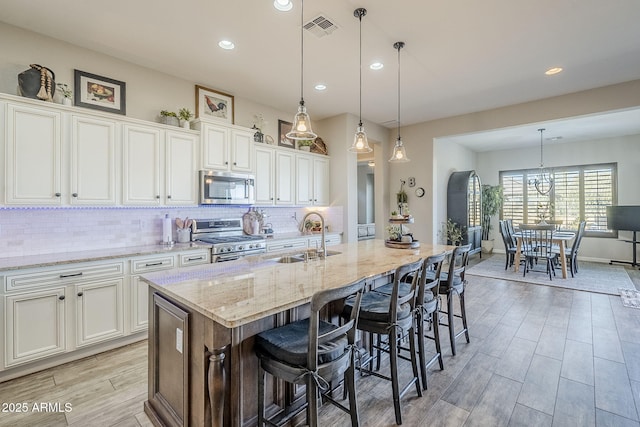 kitchen with visible vents, appliances with stainless steel finishes, a sink, light wood-style floors, and backsplash