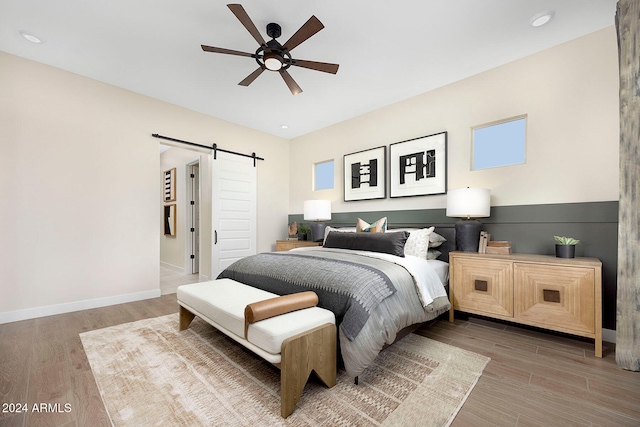 bedroom featuring ceiling fan, a barn door, and wood-type flooring