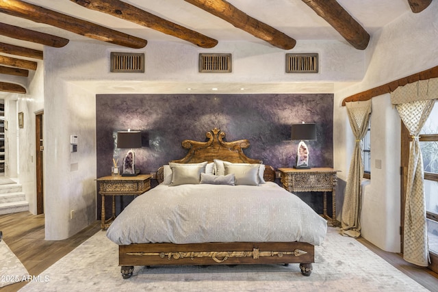 bedroom featuring beam ceiling, visible vents, and wood finished floors