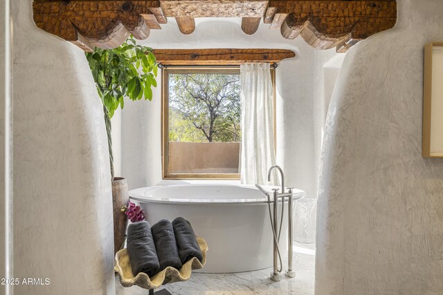 bathroom with marble finish floor and a freestanding tub