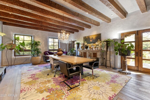 dining space with beam ceiling, french doors, light wood finished floors, and an inviting chandelier