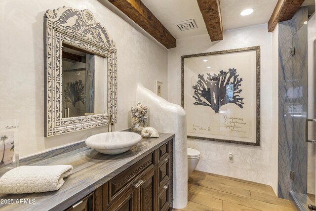 bathroom with toilet, wood finished floors, vanity, visible vents, and beam ceiling