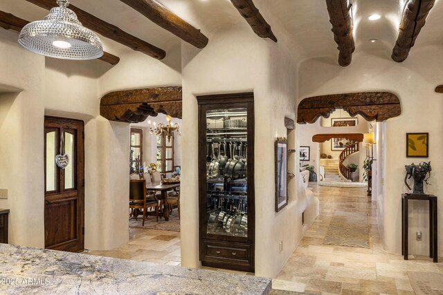 corridor featuring a chandelier, stairway, beam ceiling, and stone tile floors