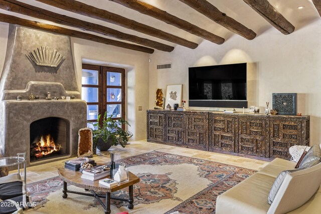 living room featuring beam ceiling, stone finish floor, a fireplace, and visible vents