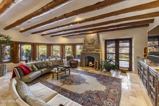 living area with a wealth of natural light, beam ceiling, a fireplace, and stone tile floors