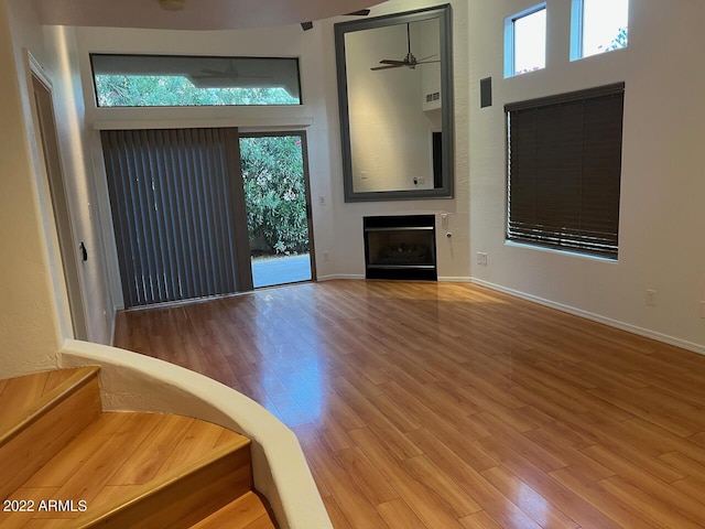 9070 E Gary Rd Unit 152, Scottsdale, AZ 85260 - unfurnished living room featuring a ceiling fan, wood finished floors, a fireplace, a high ceiling, and stairway