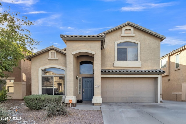 view of front facade with a garage, a tile roof, driveway, and stucco siding