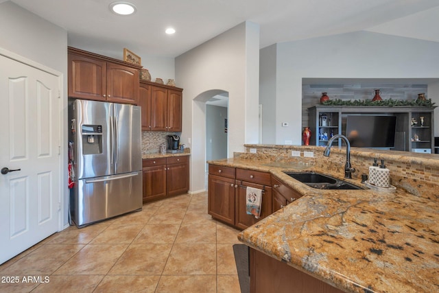 kitchen with light tile patterned floors, light stone countertops, arched walkways, a sink, and stainless steel refrigerator with ice dispenser