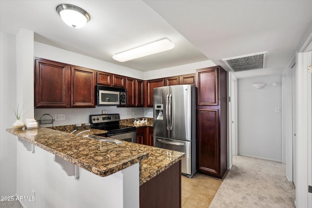 10115 E Mountain View Rd Unit 2061, Scottsdale, AZ 85258 - kitchen featuring stainless steel appliances, a peninsula, a breakfast bar area, dark stone countertops, and dark brown cabinets