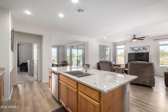 kitchen featuring dishwasher, sink, light stone countertops, a center island with sink, and light wood-type flooring