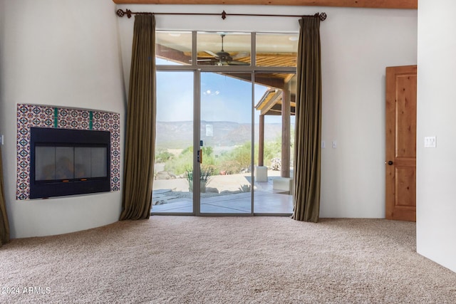 unfurnished living room with a mountain view, carpet floors, ceiling fan, and a fireplace