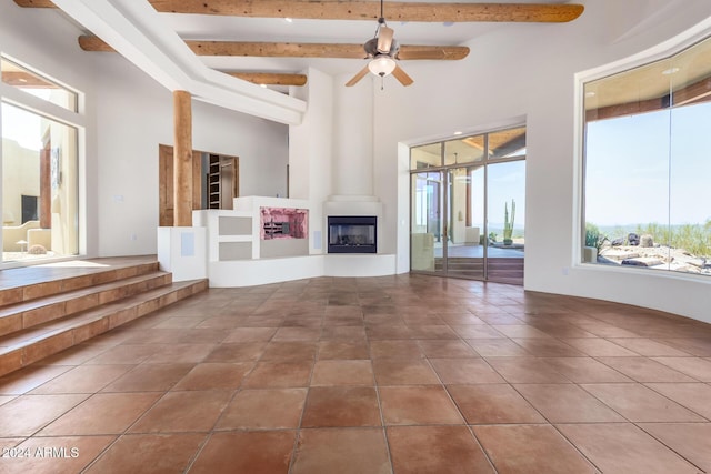 unfurnished living room with ceiling fan, a large fireplace, beamed ceiling, and tile patterned flooring