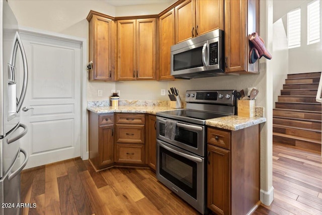 19475 N Grayhawk Dr Unit 1115, Scottsdale, AZ 85255 - kitchen with appliances with stainless steel finishes, wood finished floors, brown cabinets, and light stone countertops