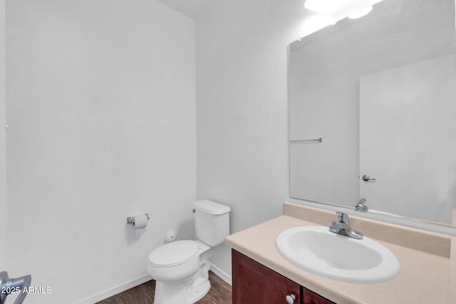 half bathroom with toilet, wood finished floors, vanity, and baseboards