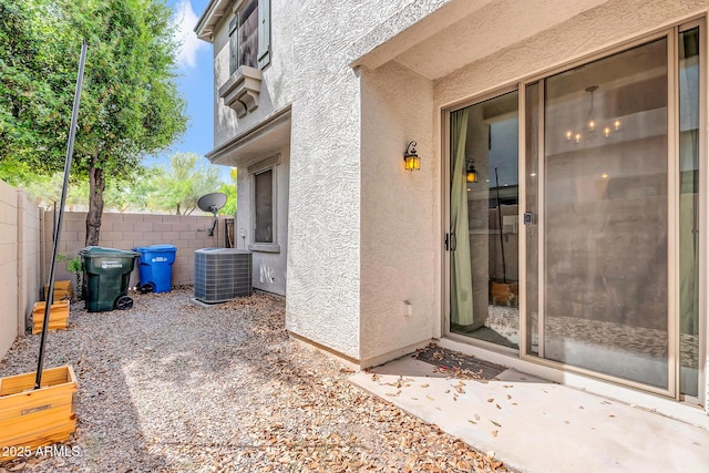 doorway to property with stucco siding, fence, and central AC