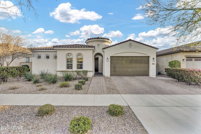 mediterranean / spanish home featuring a garage, decorative driveway, a tile roof, and stucco siding