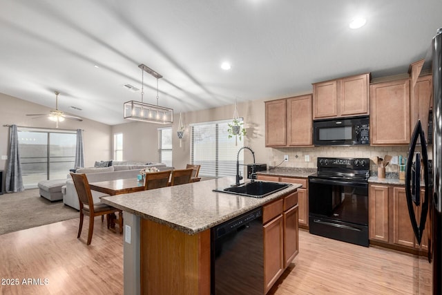 kitchen featuring decorative light fixtures, sink, black appliances, a center island with sink, and light wood-type flooring