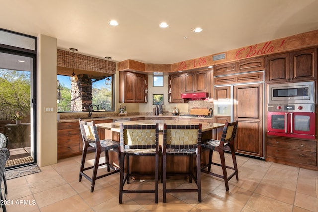 kitchen featuring a center island, built in appliances, light tile floors, and a kitchen bar