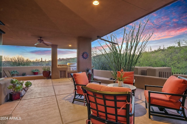 patio terrace at dusk with an outdoor living space, ceiling fan, a grill, and exterior kitchen