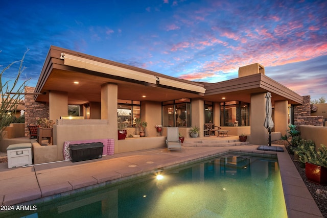 back house at dusk featuring a patio area and an outdoor fireplace