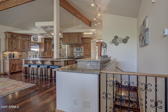 kitchen featuring brown cabinets, vaulted ceiling with beams, a breakfast bar area, and built in appliances