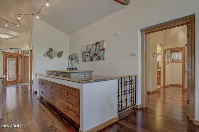 interior space featuring arched walkways, dark wood-style flooring, lofted ceiling, dark stone counters, and baseboards