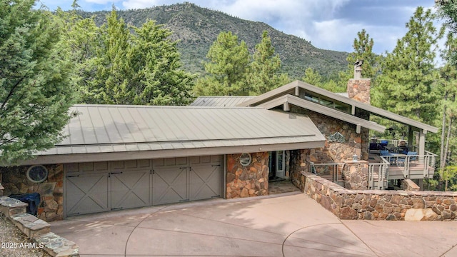 view of front facade featuring metal roof, stone siding, concrete driveway, a standing seam roof, and a chimney