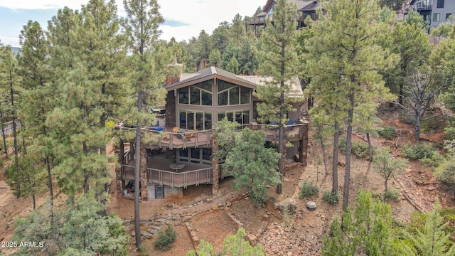 rear view of house featuring a deck, a chimney, and a forest view