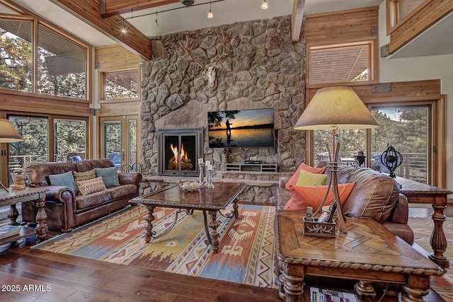 living room featuring a stone fireplace, beamed ceiling, wood-type flooring, and a high ceiling