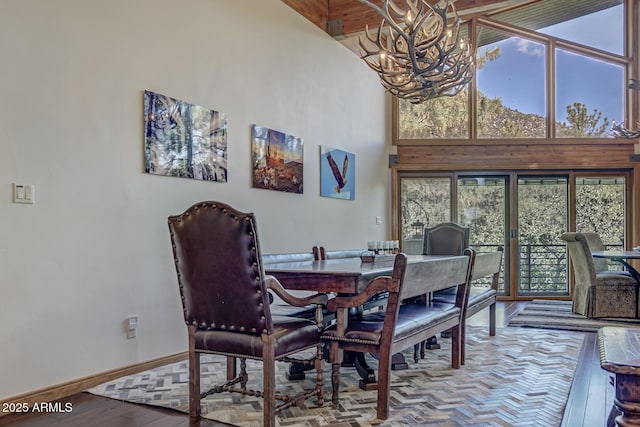 dining space with baseboards, plenty of natural light, a high ceiling, and an inviting chandelier