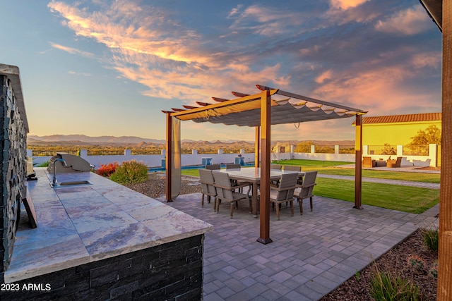 patio terrace at dusk with a water and mountain view, a pergola, and a lawn