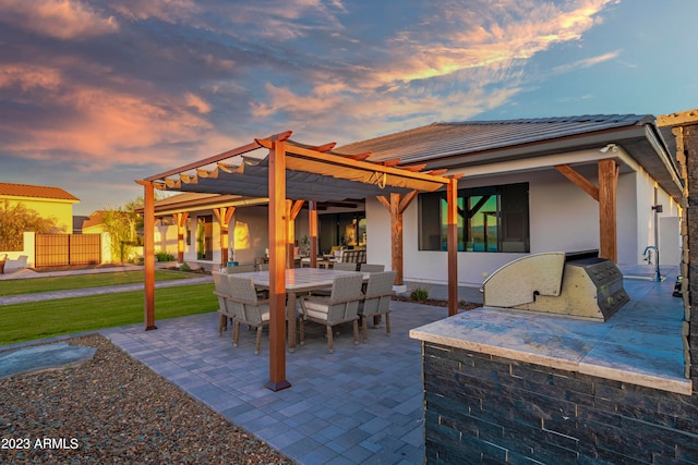 patio terrace at dusk featuring a pergola and an outdoor kitchen