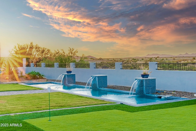 pool at dusk featuring a lawn and pool water feature